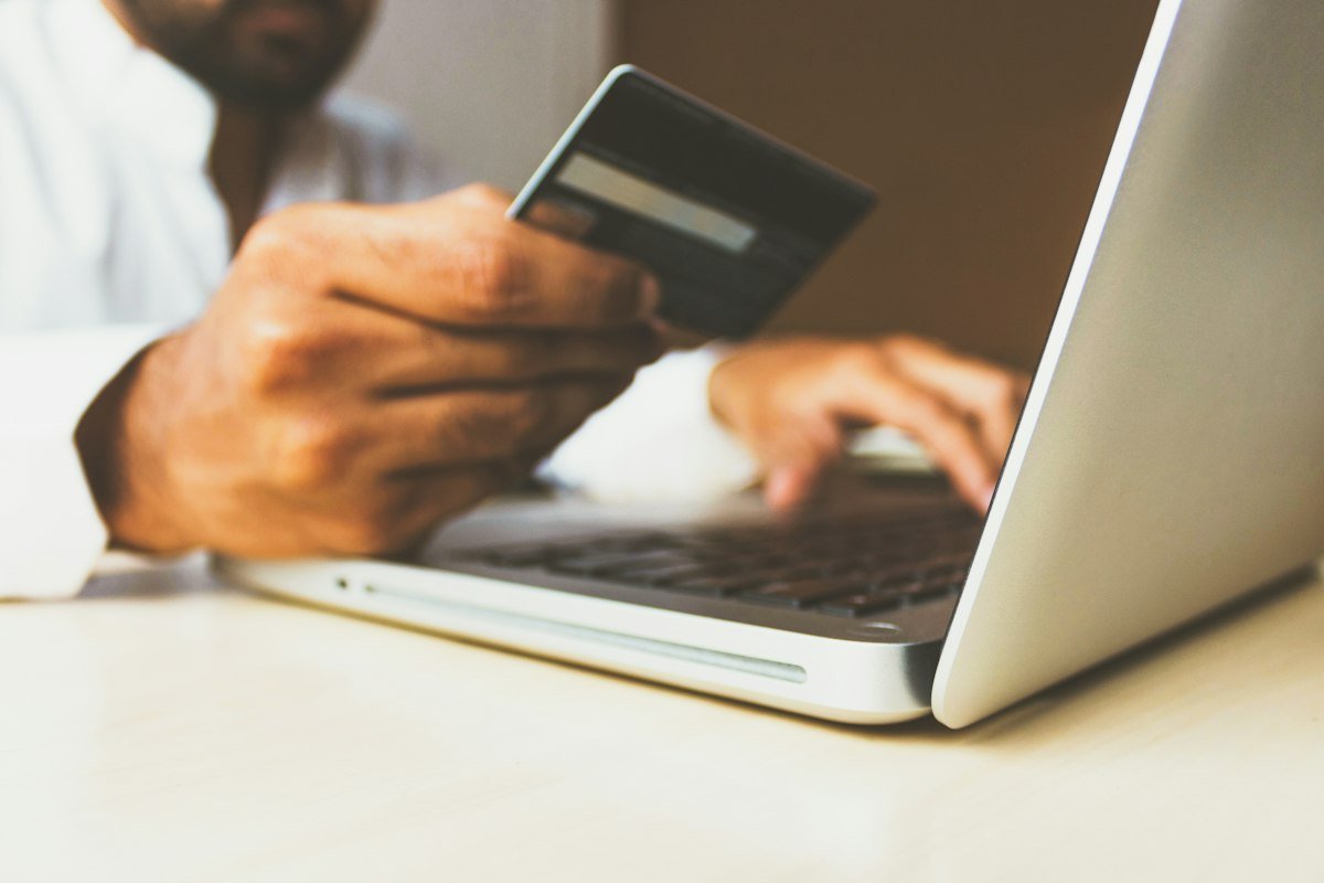 Person holding a credit card while using a laptop for online shopping