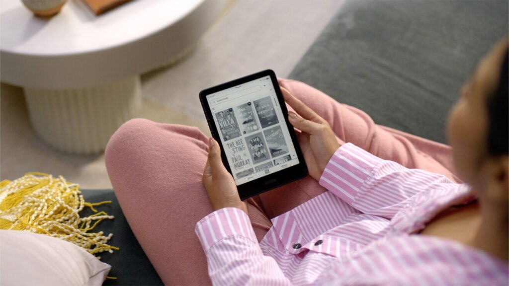 Reader holding a Kindle Paperwhite at home with book covers on screen